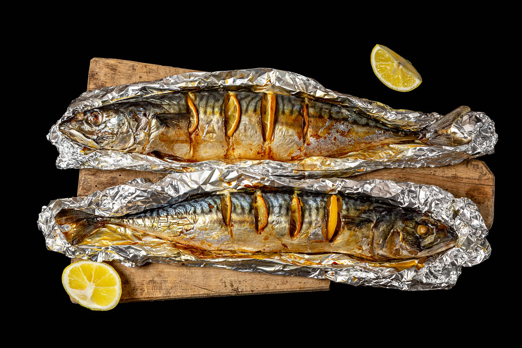 Two baked mackerel with lemon slices in foil, top view