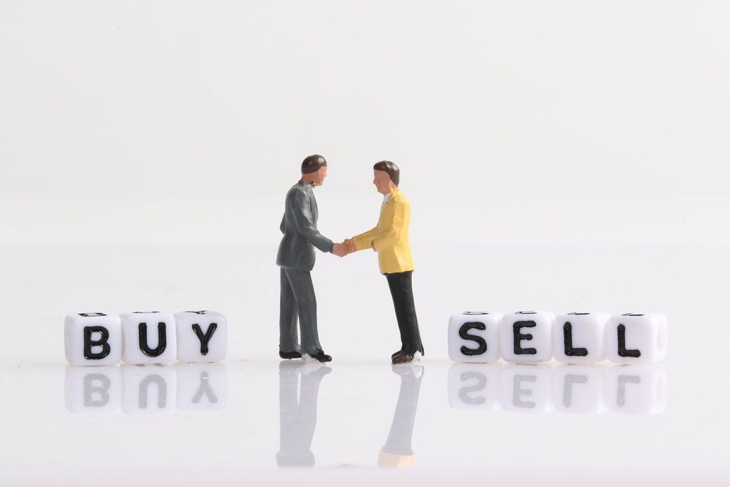 Two businessman shaking hands in front of Buy and Sell text