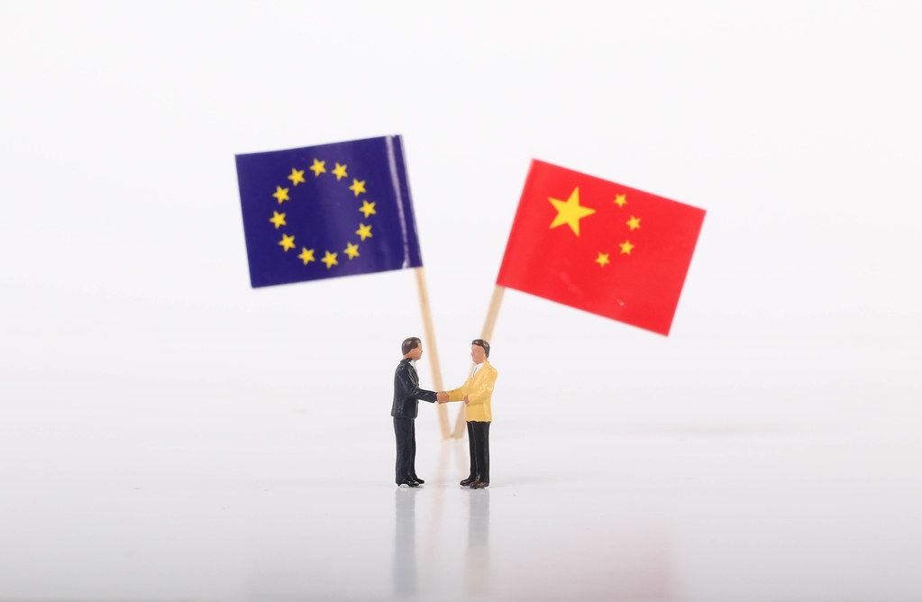 Two businessman shaking hands in front of flags of European Union and China