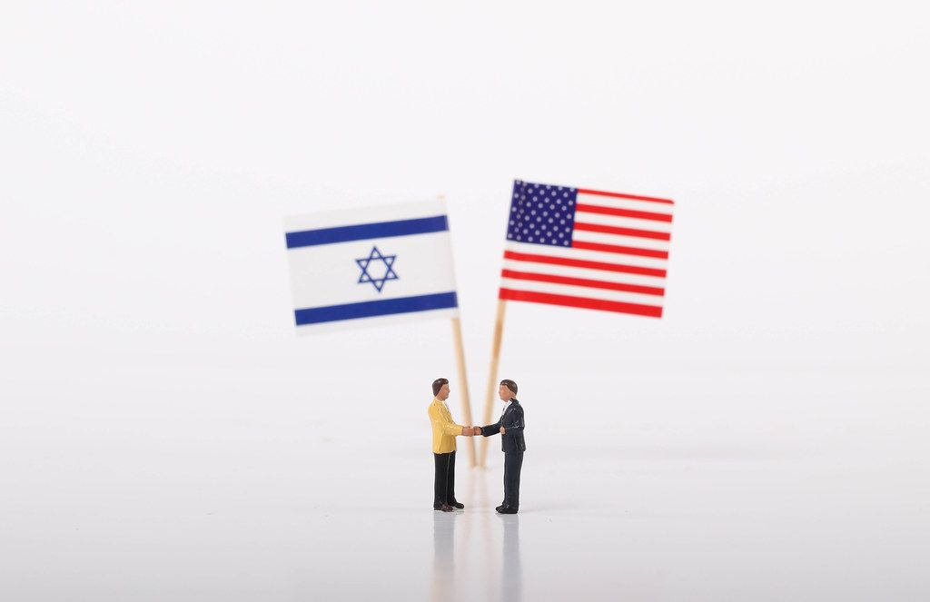 Two businessman shaking hands in front of flags of Israel and USA