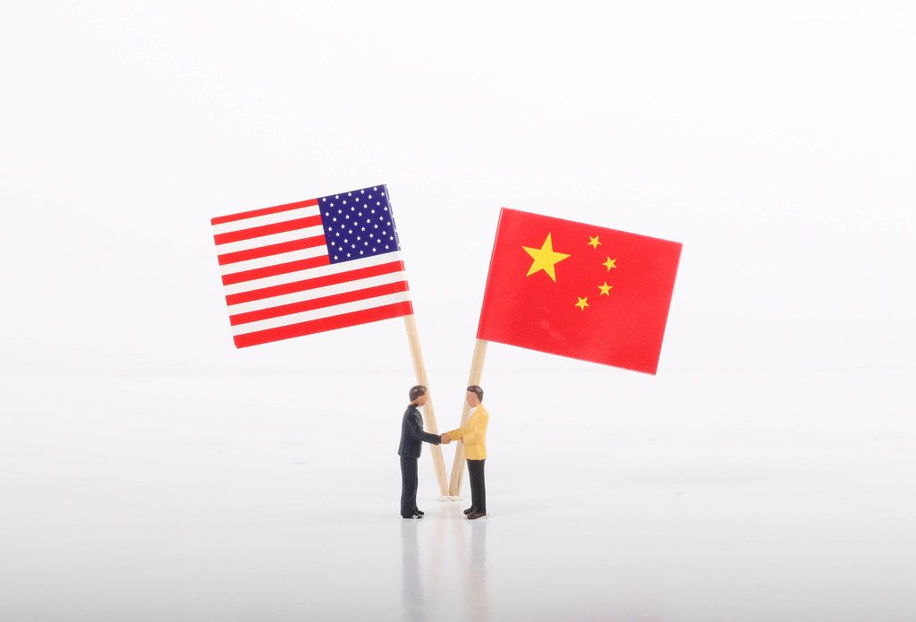 Two businessman shaking hands in front of flags of USA and China on white background