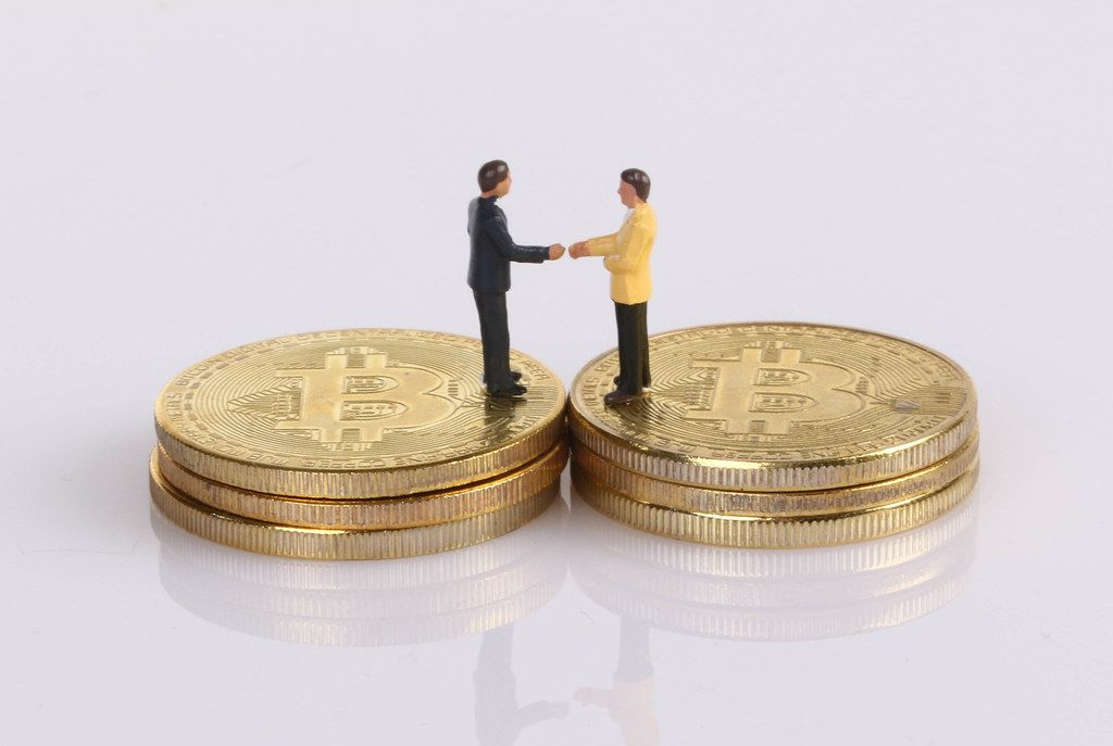 Two businessman shaking hands while standing on golden Bitcoins