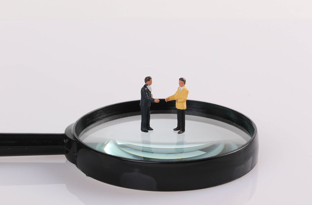 Two businessman shaking hands while standing on magnifying glass