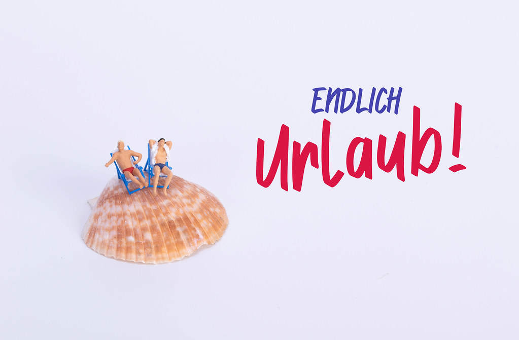 Two man sitting in deck chairs on sea shell with Endlich Urblaub text