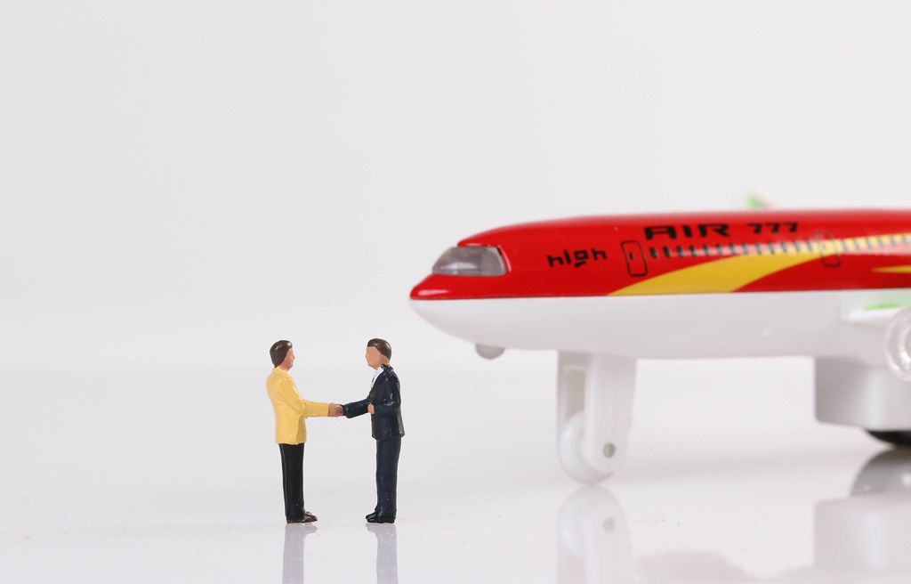 Two miniature businessman shaking hands near airplane