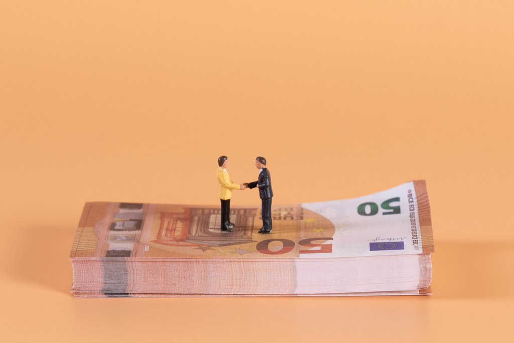 Two miniature businessman shaking hands on a stack of Euro money