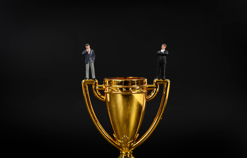 Two miniature businessman standing on golden trophy