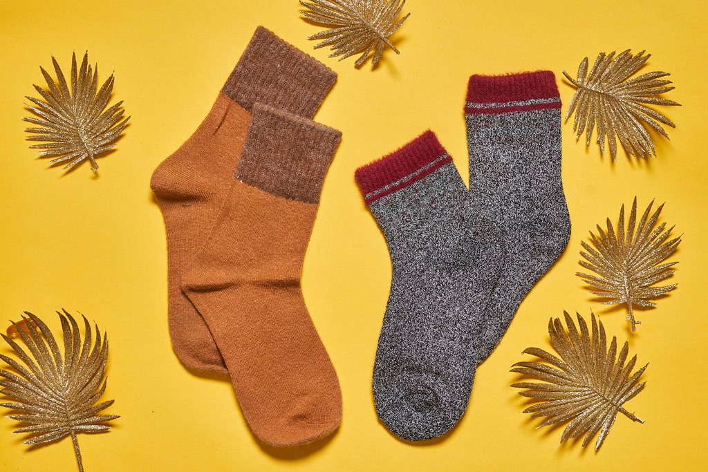 Two pairs of warm socks on yellow background with autumn leaves - for her and for him
