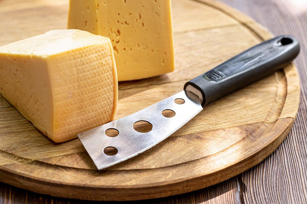 Two pieces of cheese and a cheese knife on a wooden kitchen board