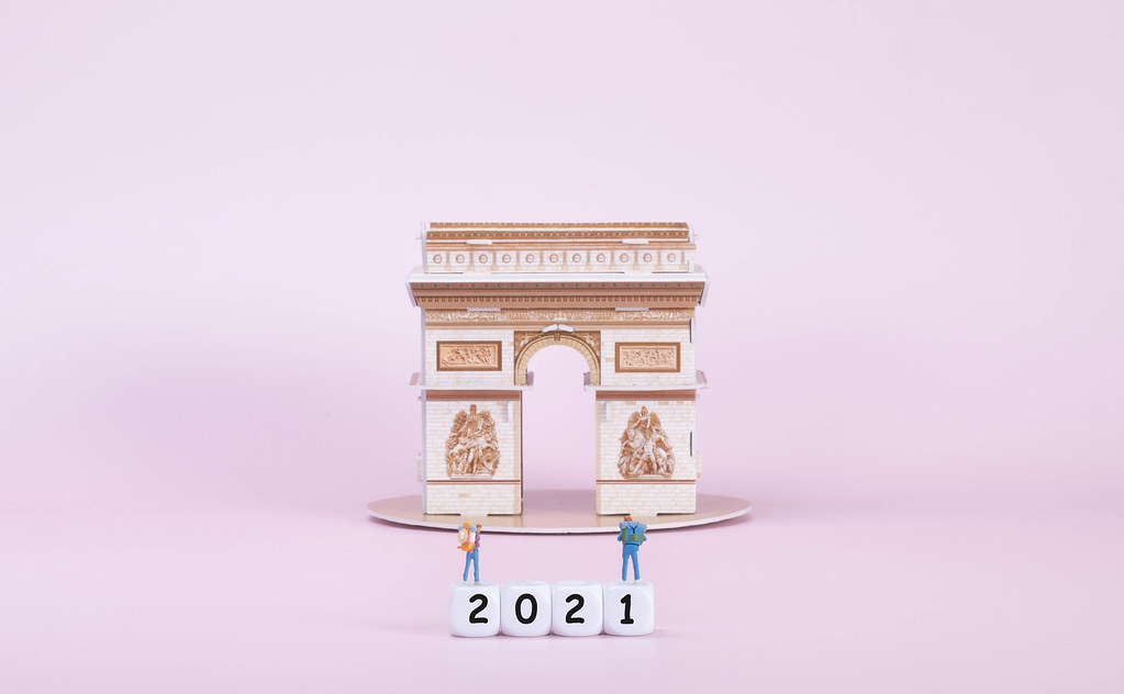 Two travelers standing on blocks with 2021 text in front of Arc de Triomphe