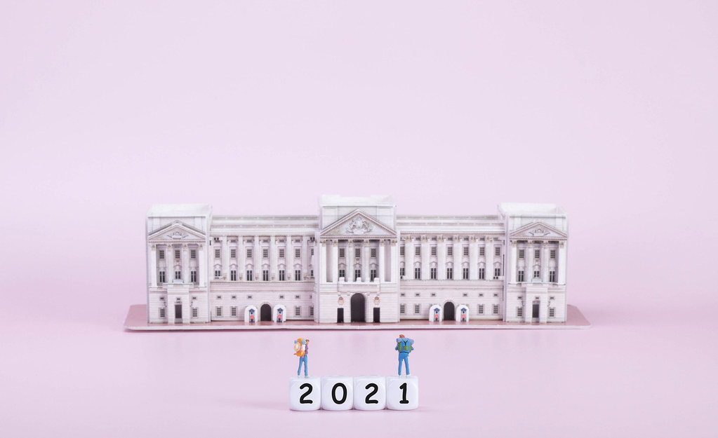 Two travelers standing on blocks with 2021 text in front of Buckingham palace