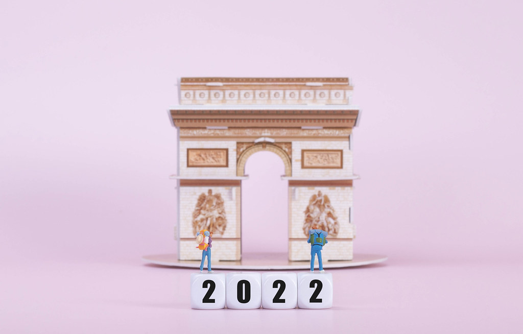 Two travelers standing on blocks with 2022 text in front of Arc de Triomphe