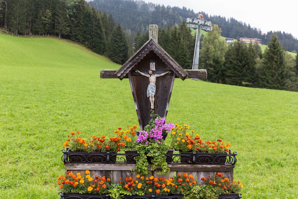 Typisches hölzernes Wegkreuz mit Blumen in Alpbach, Tyrol
