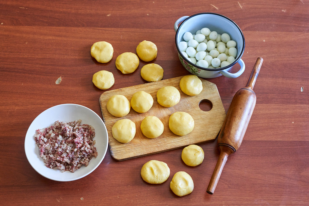 Uncooked dumpling dough with bowls of minced meat and quail eggs