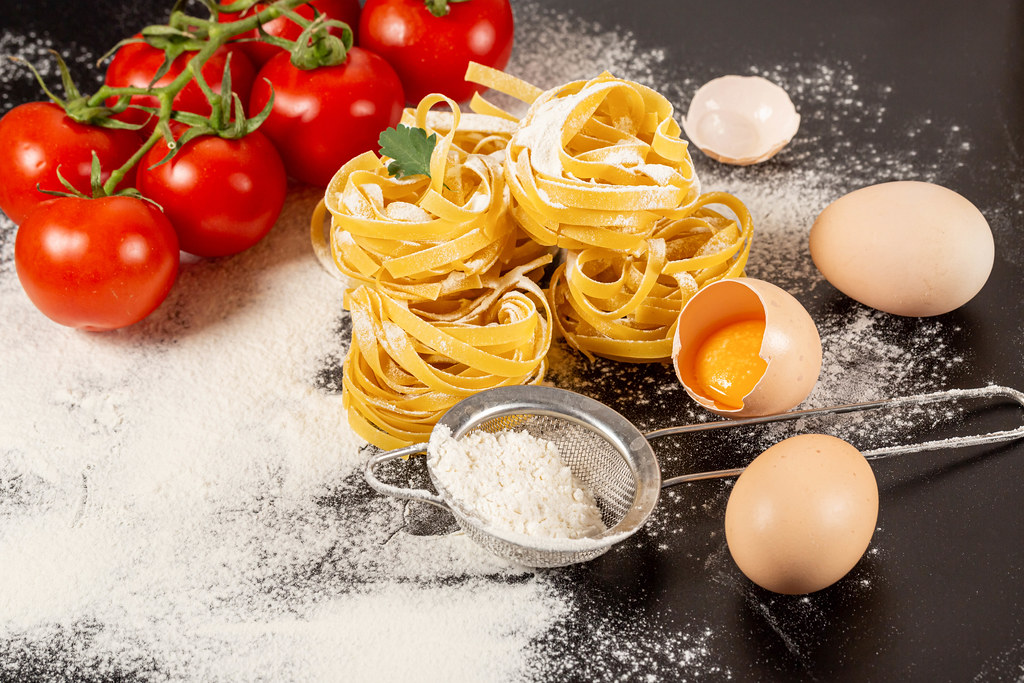 Uncooked rolled traditional italian pasta on dark background with tomatoes, eggs and flour