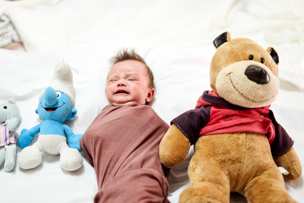 Unhappy baby boy lying between plush toys