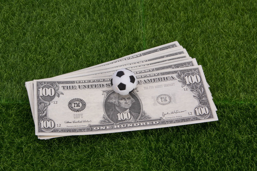 US dollar banknotes with soccer ball on green grass