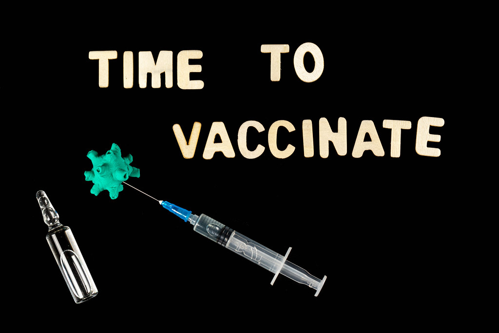 Vaccine ampoule and syringe with virus model on dark background, time to vaccinate text