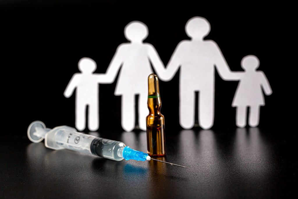 Vaccine and syringe on dark background with family silhouette behind