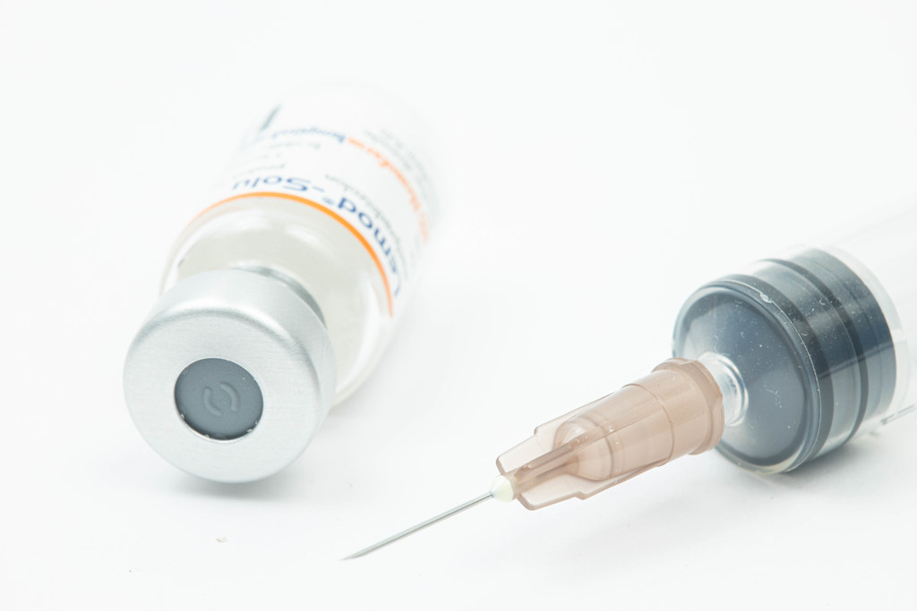 Vaccine bottle with injection needle above white background