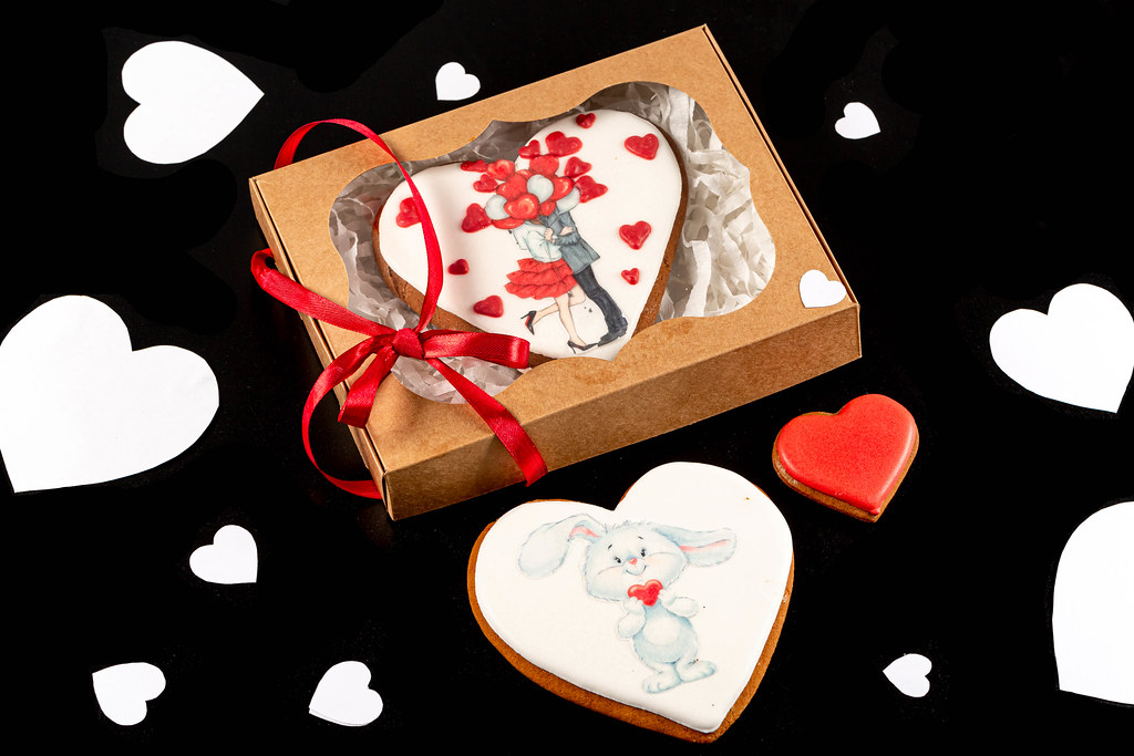 Valentines day cookies in gift box on black background with paper hearts