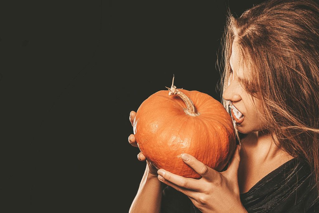 Vampire girl with fangs holding a pumpkin near the face