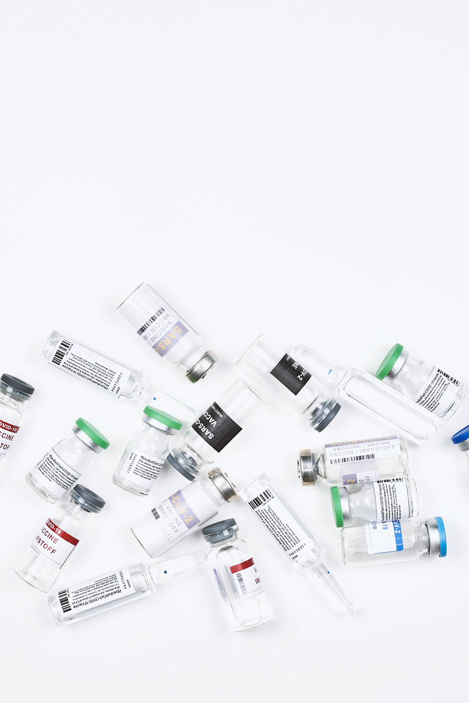 Viele verschiedene Ampullen mit Covid-19 Impfstoff vor weißem Hintergrund mit Platz für Text