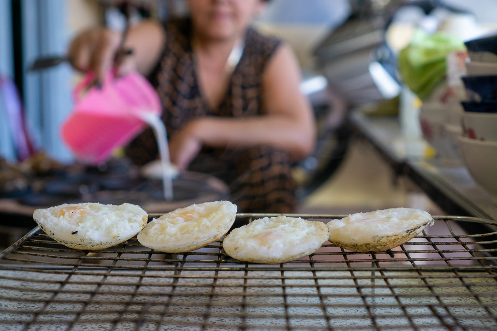 Vietnamese Banh Can Rice Cakes on a Barbecue Grill Grid with Vietnamese Woman Preparing Food in the Background in Da Lat, Vietnam