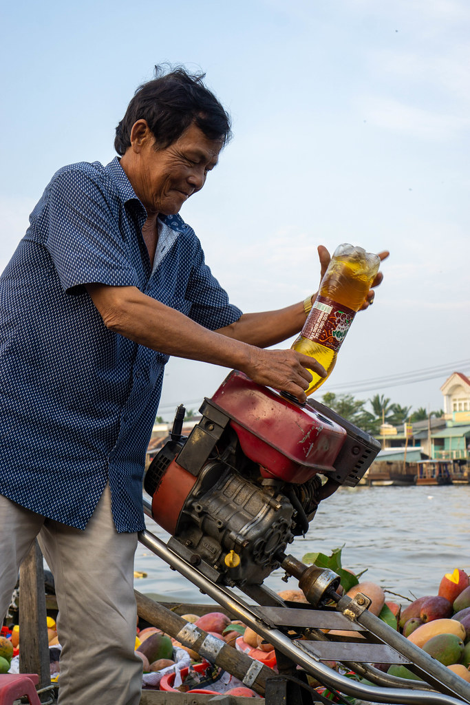 Vietnamese Man fueling an Engine of a Motorboat with Gasoline from Water Bottle at Cai Rang Floating Market in Can Tho, Vietnam