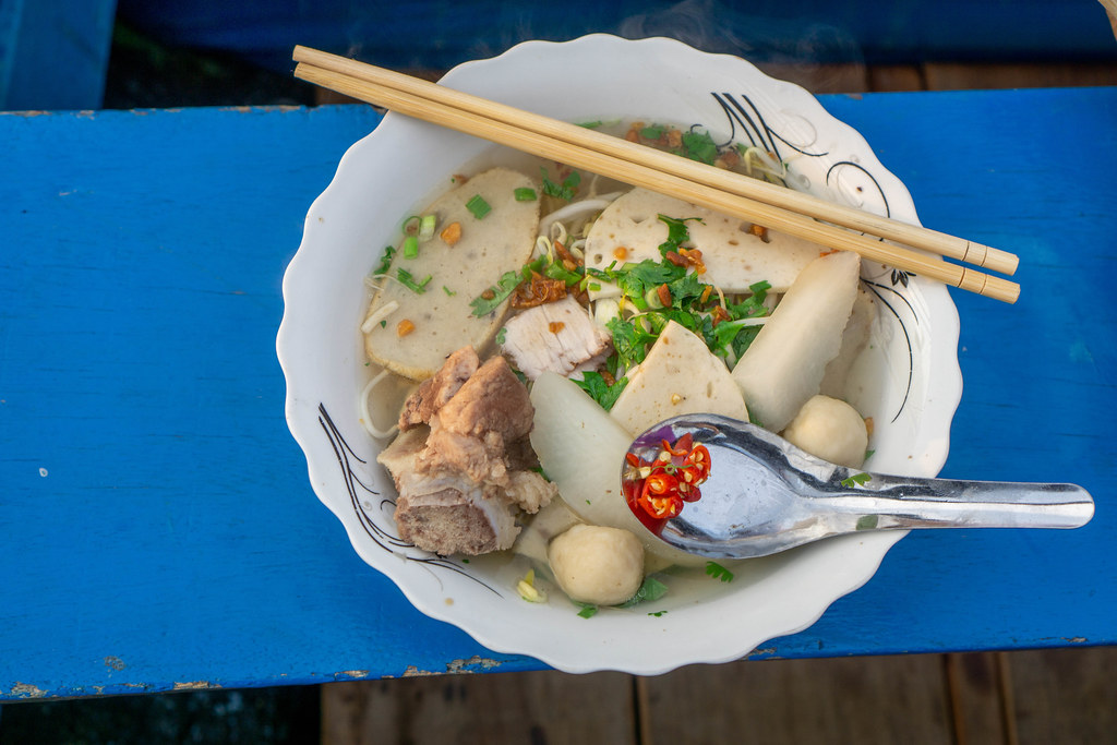 Vietnamese Noodle Soup Hu Tieu with Meatballs, Pork Ham, Pork Meat, Vegetables and Chili in a Bowl with Chopsticks and Spoon on a Boat at Cai Rang Floating Market in Can Tho, Vietnam