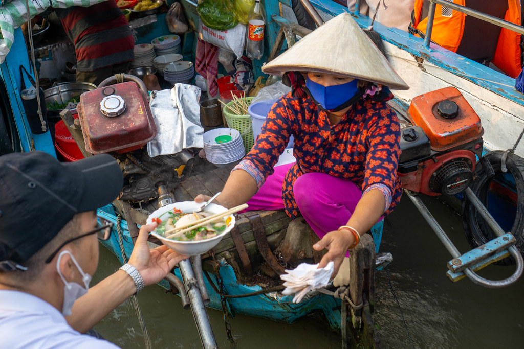 Vietnamese Woman delivering a Bowl of Hu Tieu Noodle Soup from a Boat Restaurant to another Boat at Cai Rang Floating Market in Can Tho, Vietnam