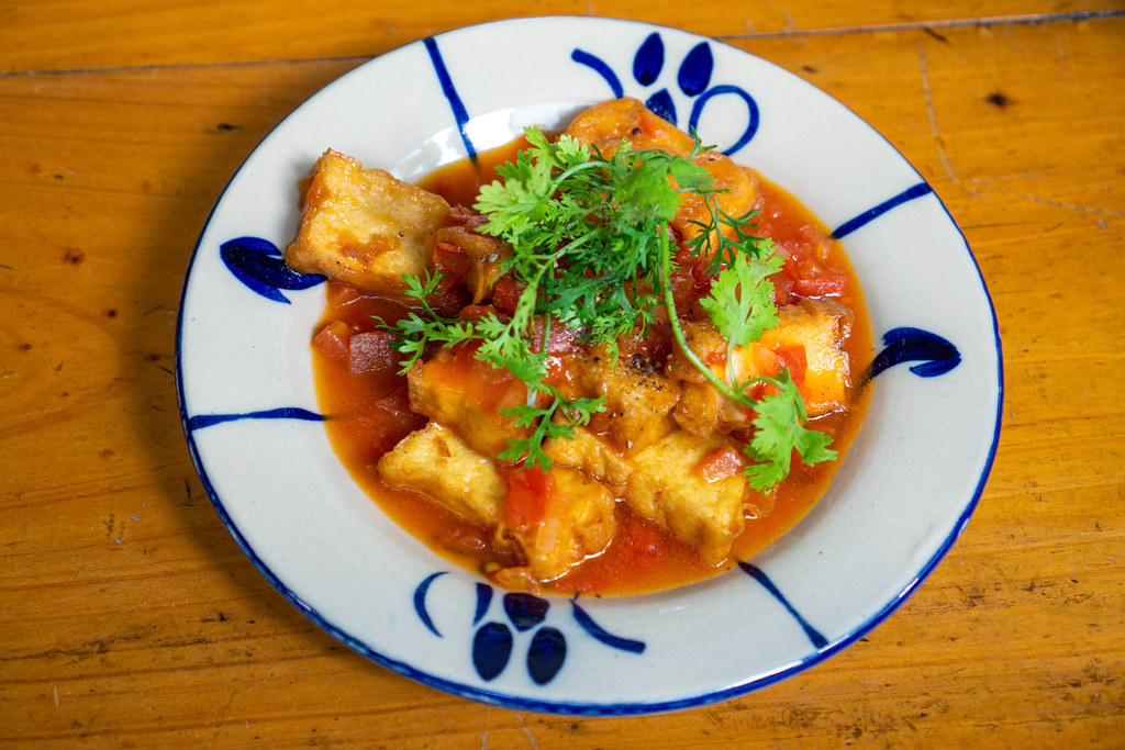 Vietnamesisches Gericht mit Tofu, Tomatensauce, Petersilie und Gewürzen auf einem Teller in einem Restaurant