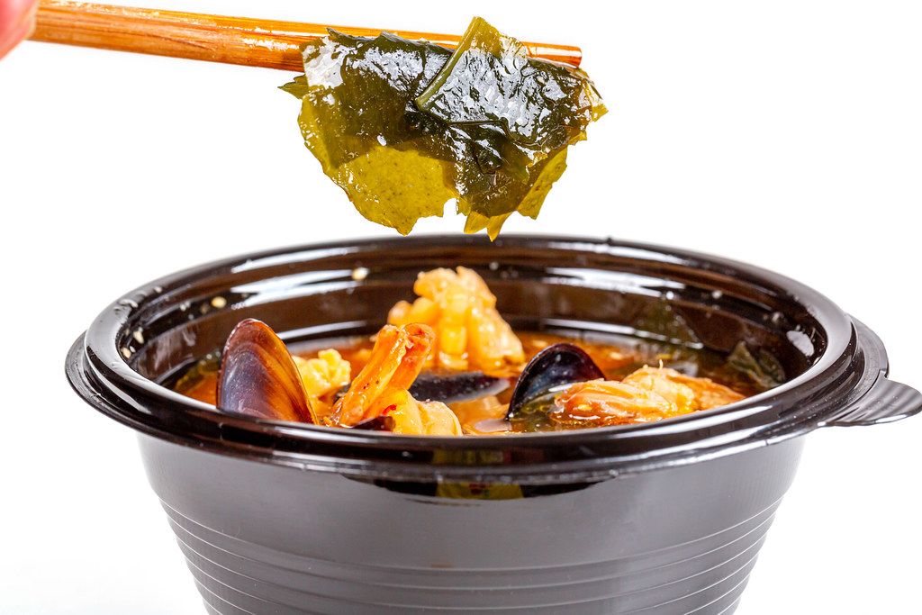 Wakame seaweed in wooden chopsticks and a bowl of miso soup