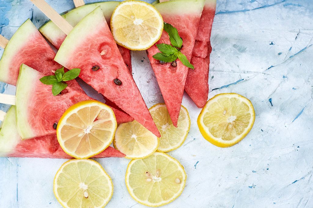 Watermelon pieces with wooden sticks and lemon slices on bright background