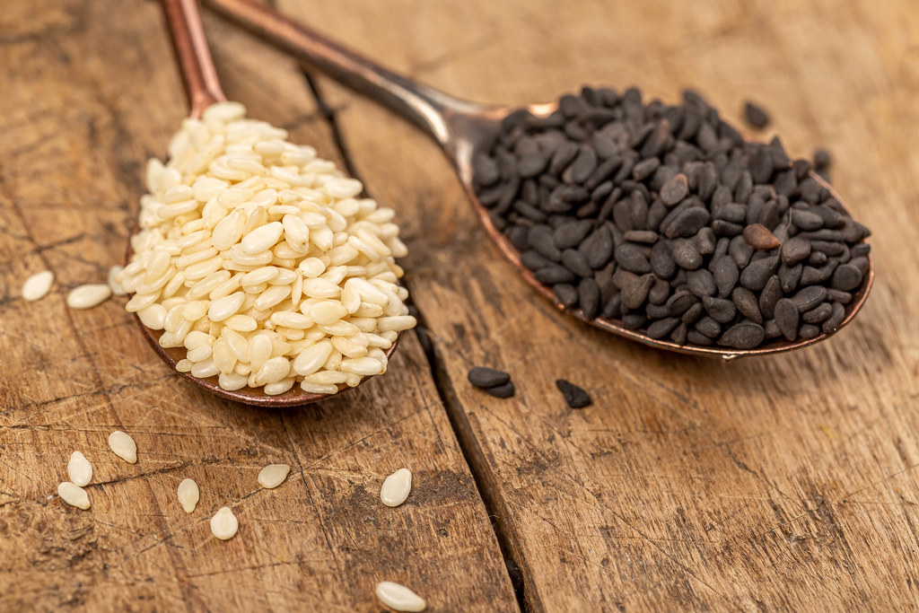 White and black sesame seeds in spoon on old wooden background