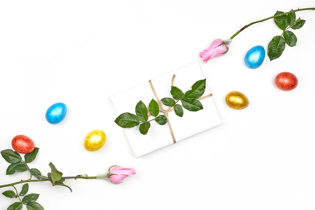 White background for Easter with copy space, with dyed eggs, roses and a gift decorated with leaves
