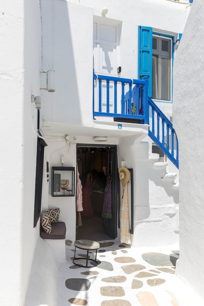 White houses with blue railings and windows and a clothes shop in a bright, white alley of Mykonos