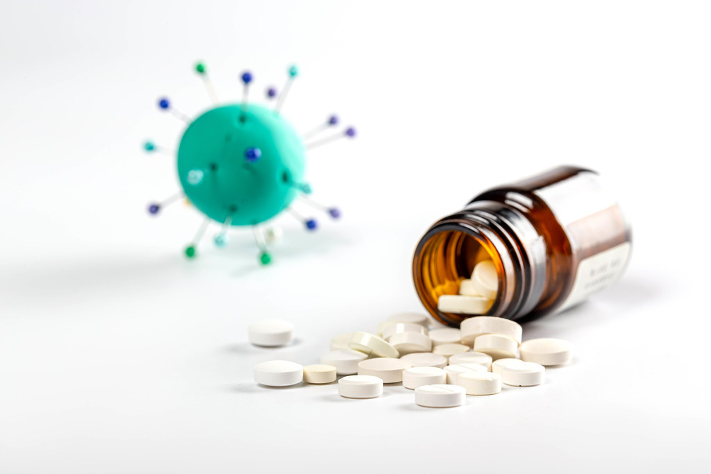 White pills sprinkled from bottle on white background with coronavirus model