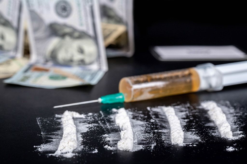 White powder sprinkled on a black background, behind money and a syringe with a drug