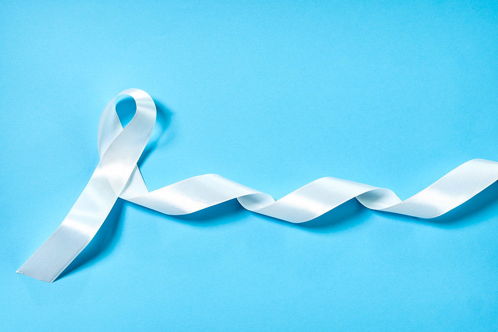 White ribbon as symbol of woman violence or lung cancer on blue background
