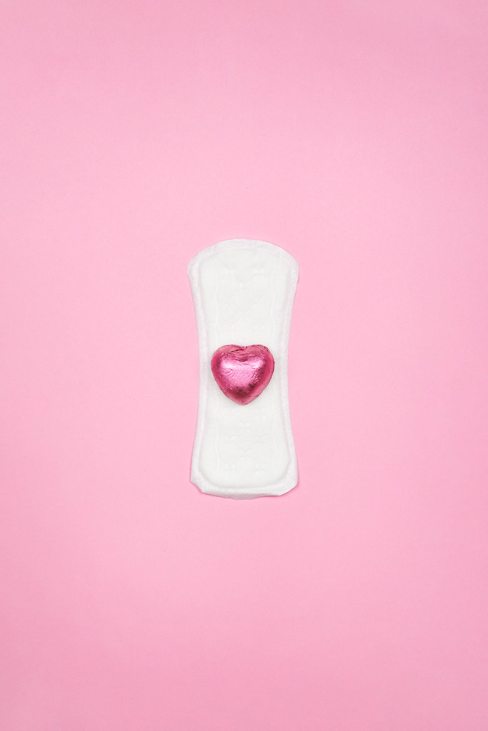 White sanitary napkin with a pink candy on bright color background