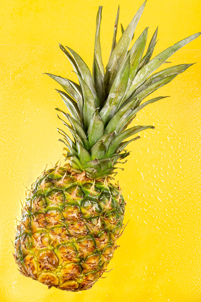 Whole sweet fresh pineapple on yellow with water drops
