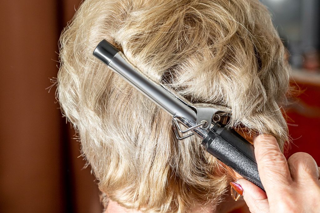Woman at home doing hair styling with an electric curling iron