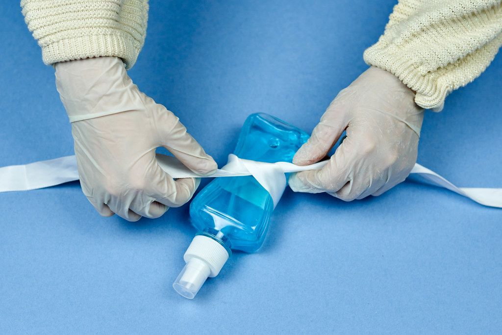 Woman bowing white ribbon on hand sanitizer bottle
