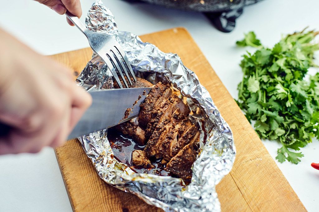 Woman cutting freshly baked chicken meat in foil