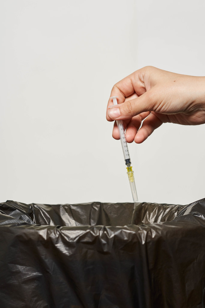 Woman hand throwing a syringe into the garbage bin against white background