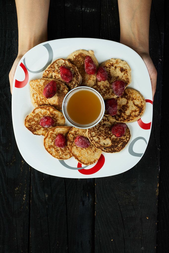 Woman hands holding a plate of oatmeal pancakes with strawberry and honey