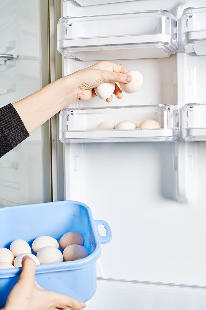 Woman holding a bowl of eggs and putting them into the refrigerator shelve