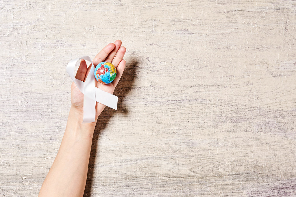 Woman holding a miniature glove and white cancer awareness ribbon over the wooden background with copy space