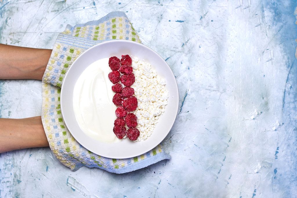 Woman holding a plate of healthy dieting breakfast - cottage cheese and sour cream with raspberries
